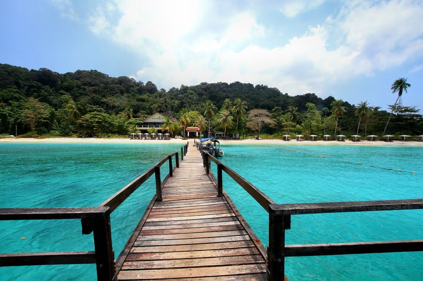 Wooden jetty over turquoise water leading to a palm-lined beach on Pulau Lang Tengah.