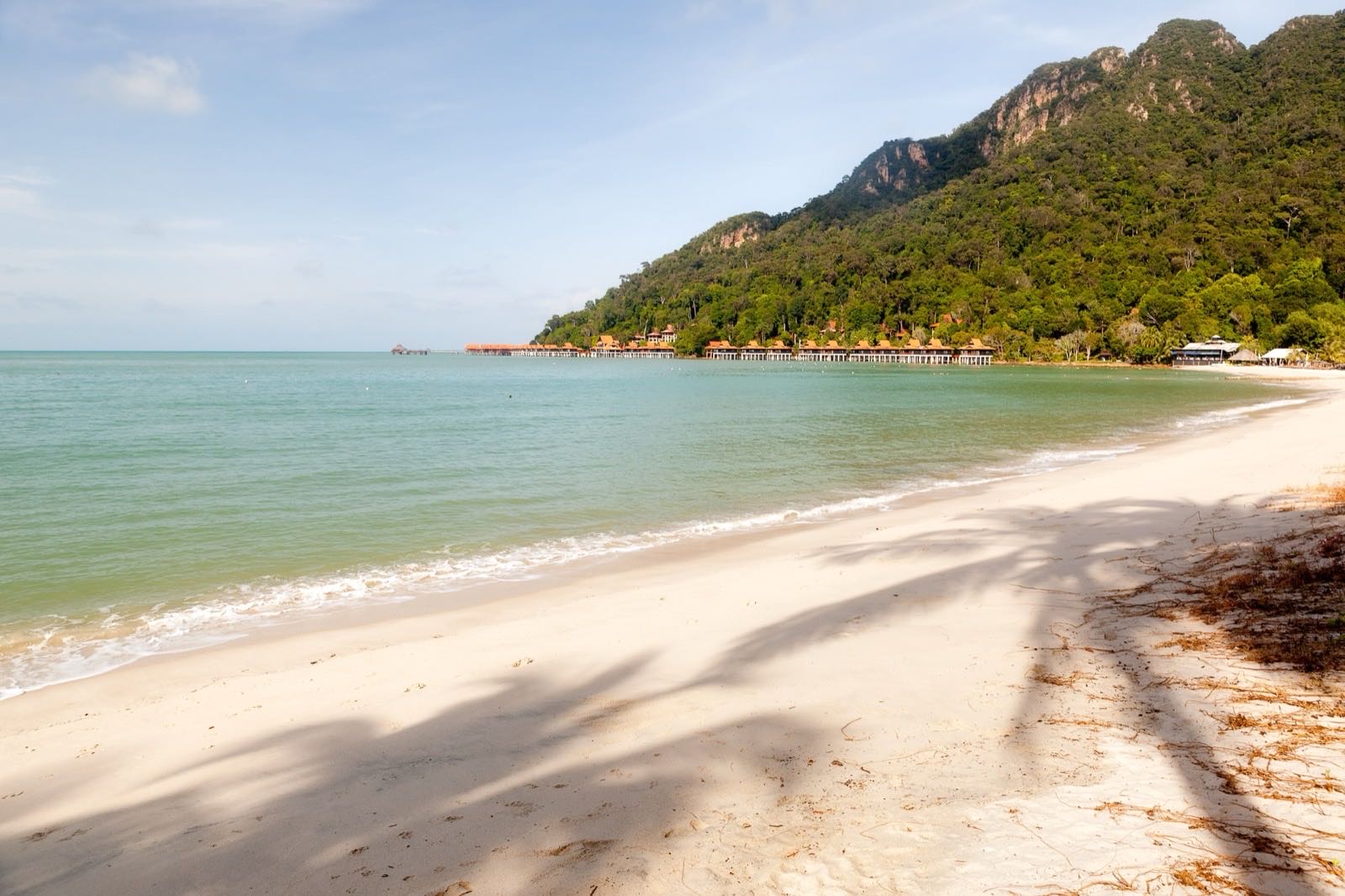 Empty white-sand beach and calm green sea below forested hills on Langkawi.
