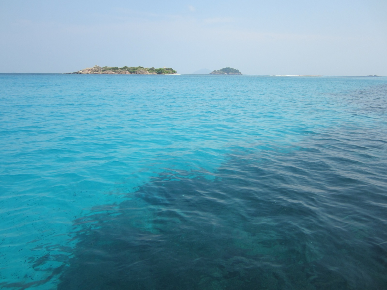 Clear turquoise water over coral off Pulau Redang, with small islets on the horizon.