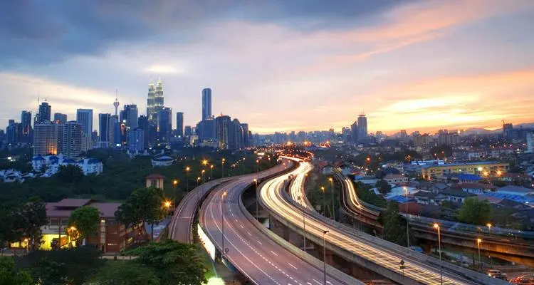 Vue d’une autoroute menant à Kuala Lumpur avec la skyline de la ville en arrière-plan, illustrant l’excellente infrastructure routière de la Malaisie.
