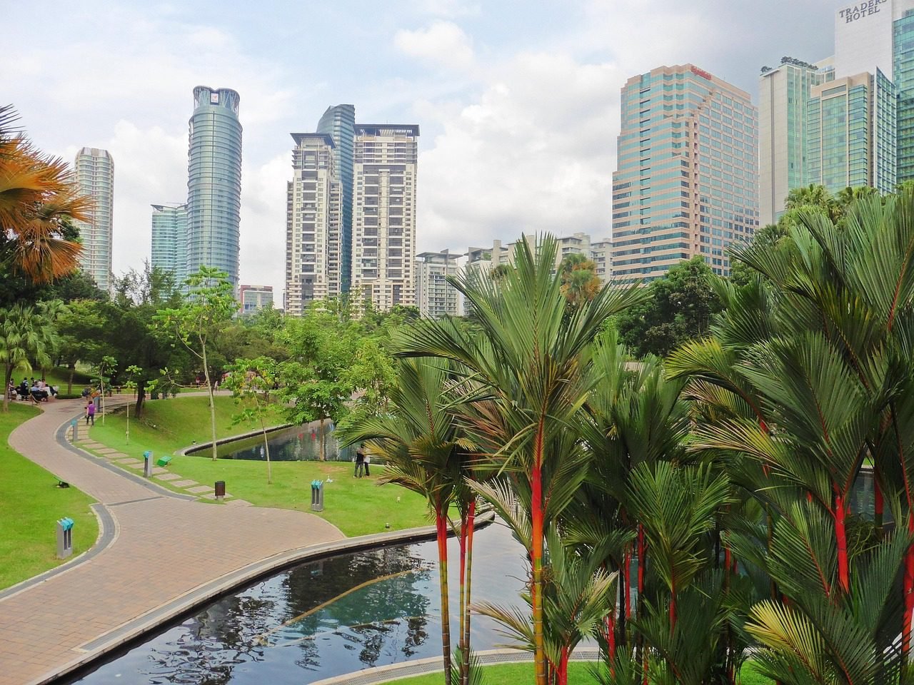 KLCC Park in Kuala Lumpur with tropical palm trees, walking paths, and high-rise buildings in the background.